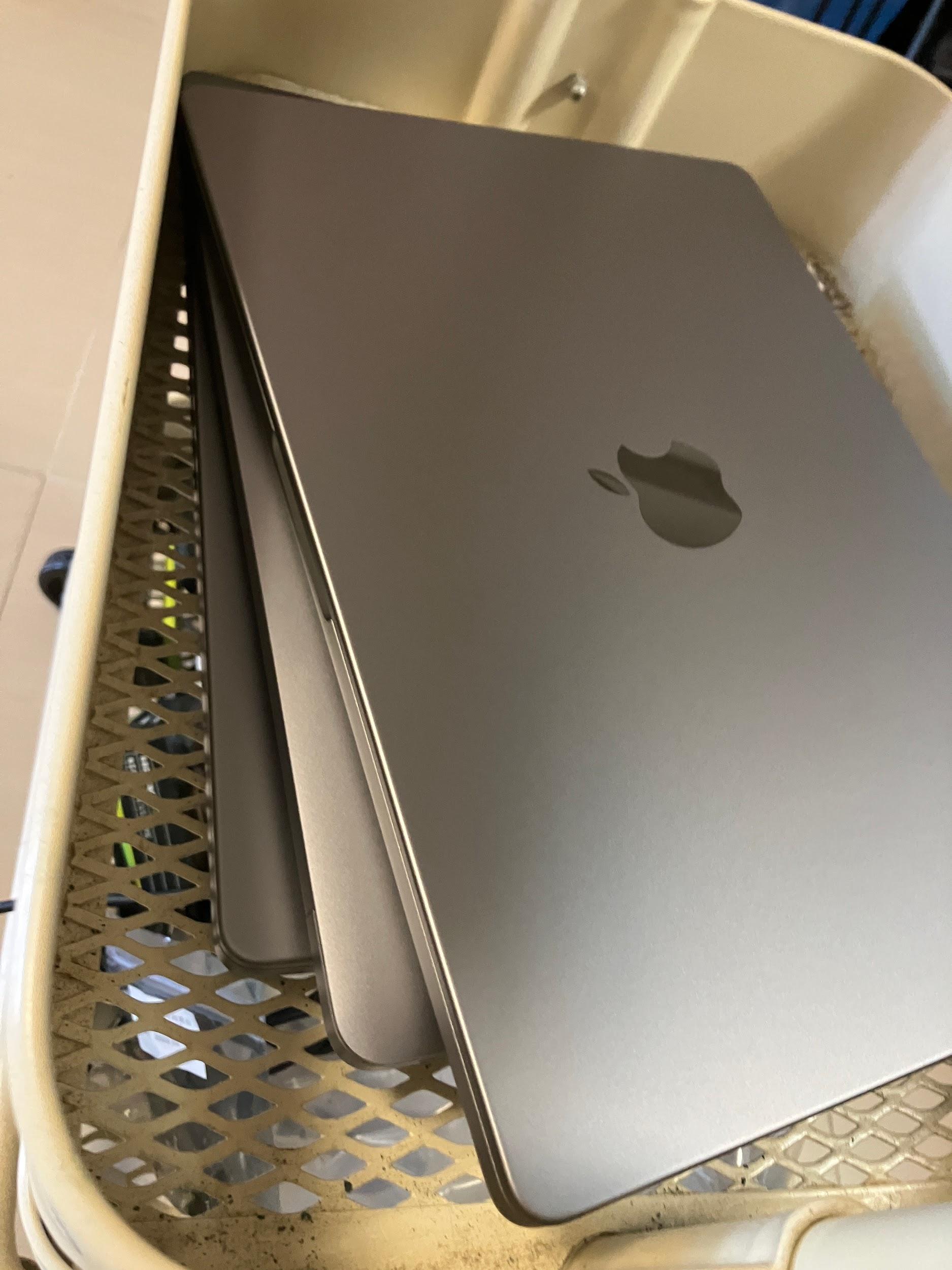 A stack of silver Mac laptops arranged in a laboratory storage cart